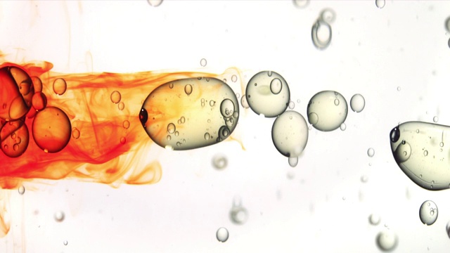 特写慢镜头，橙色的墨水从左边流入，一排油泡在白色的背景上跳跃视频素材