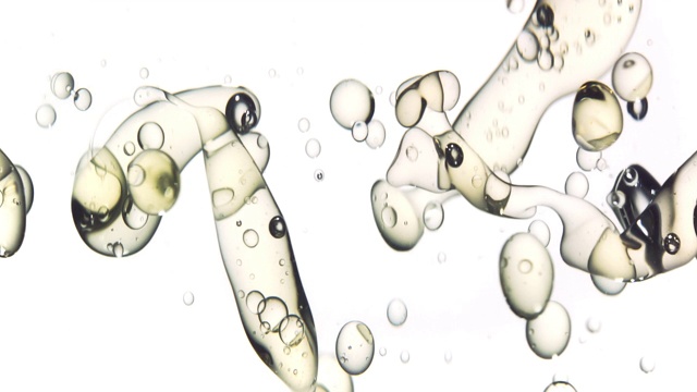 近距离和缓慢的运动倾倒黄金油从右和创造一排泡沫水下，而弹跳在白色的背景视频素材