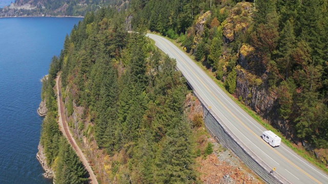 航拍:在阳光明媚的日子里，在高速公路上行驶的车辆经过树木和峡湾——不列颠哥伦比亚省狮子湾视频素材