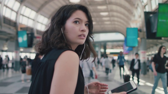 一名日本女子戴着耳机和智能手机在东京火车站转弯视频下载