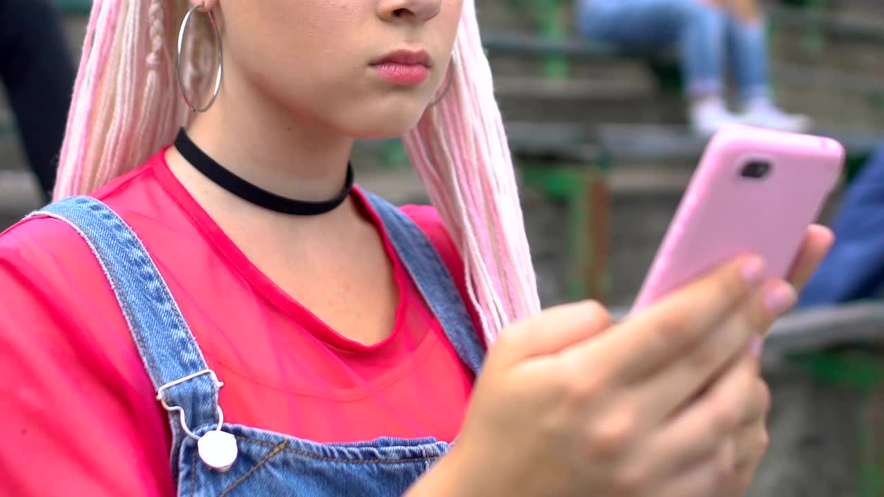 年轻的白人时尚女孩在楼梯上滚动智能手机，科技视频下载