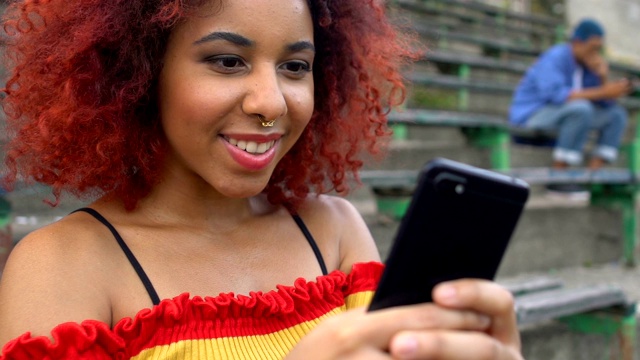 兴奋的红发年轻女性戴着鼻环看手机视频，应用程序视频下载