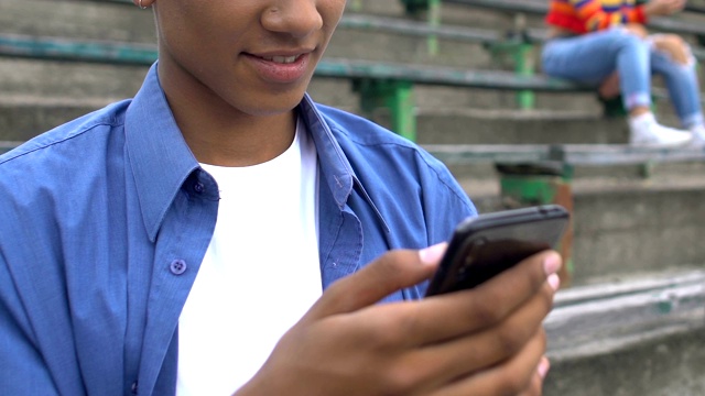 放松的非裔美国男性青少年看恶作剧视频在手机上和微笑视频下载