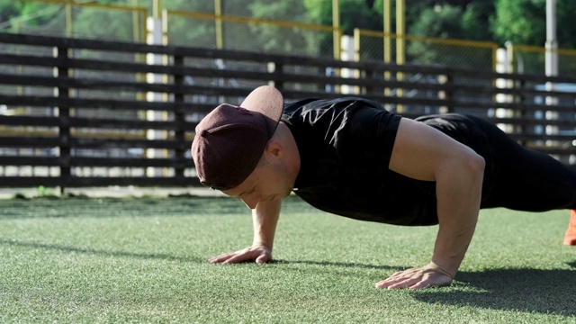 一个年轻人在绿色操场上做俯卧撑。做俯卧撑的运动员视频素材