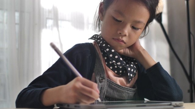 小女孩在数字平板电脑上写家庭作业，用于学习和教育视频下载