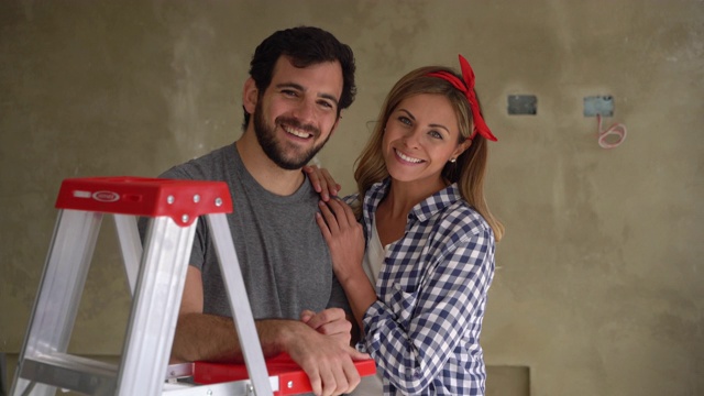幸福的年轻夫妇做一个家庭装修倚在梯子对着镜头微笑视频素材
