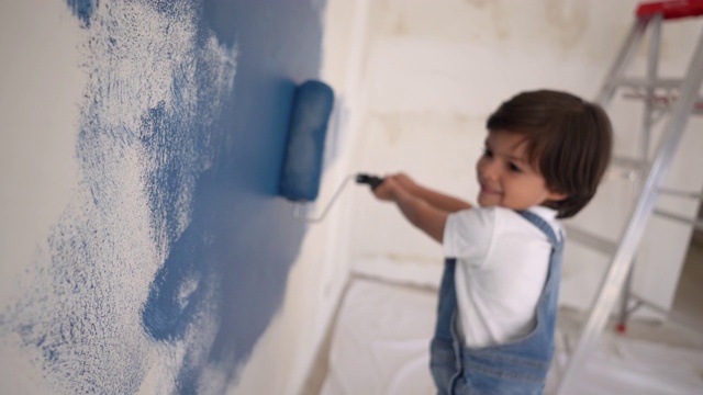 可爱的小男孩喜欢在家里用油漆滚筒画画，面带微笑视频素材