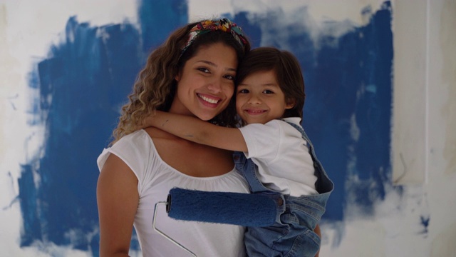 在家庭装修项目中，慈母抱着她的儿子和一个油漆滚筒，对着镜头微笑视频素材