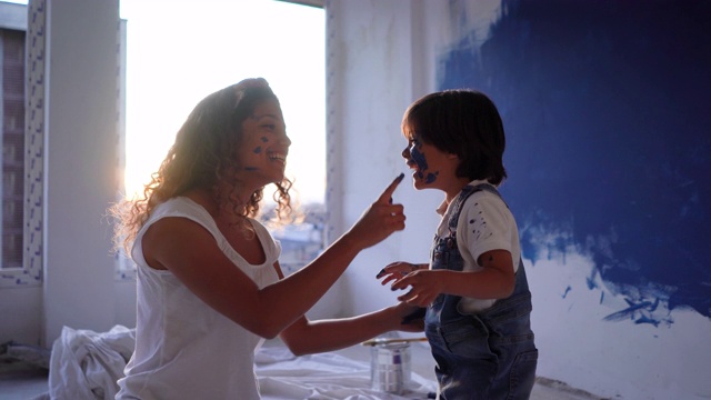 拉丁美洲的母亲和儿子在一个家庭装修油漆油漆他们的脸，非常好玩的一团糟视频素材