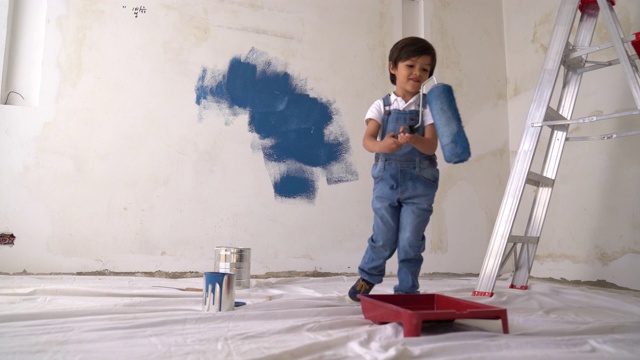 一个可爱的小男孩在家里用油漆滚筒帮忙自己动手画视频素材