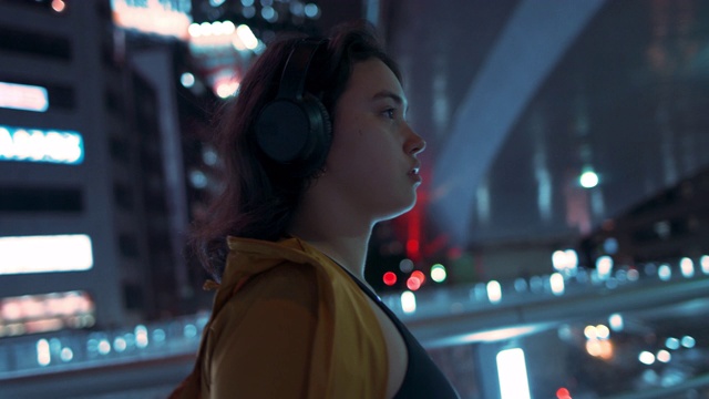 日本东京，一名年轻女子戴着耳机在桥下行走视频购买