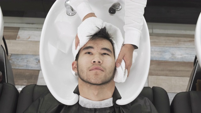 摄像俯视图亚洲男子的美发师为客户洗头视频下载