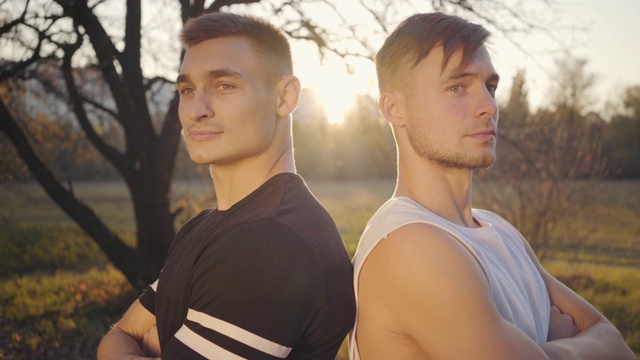 两个年轻的白人健美运动员站在阳光下看着镜头的特写。英俊强壮的运动员花时间在秋天公园。健康的生活方式，运动的理念。视频素材
