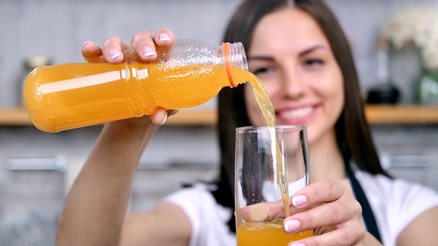 特写微笑的女孩倒清新的维生素橙汁到玻璃杯享受健康的生活方式视频下载