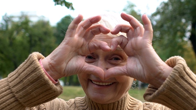 幸福的女人在她70岁的时候用手表示爱心，象征着爱，特写视频下载
