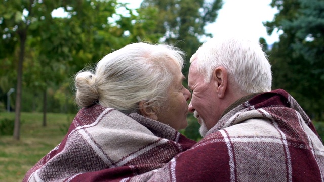 一对年长的夫妇坐在格子裙下的长凳上，成熟的女人亲吻着男人的脸颊视频素材