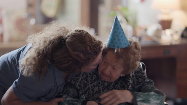 孙女在她的100岁生日聚会上，在打开礼物的间隙亲吻她的祖母的脸颊视频下载