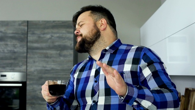 快乐和快乐的胖大胡子男人喝着咖啡，在厨房里慢舞视频素材