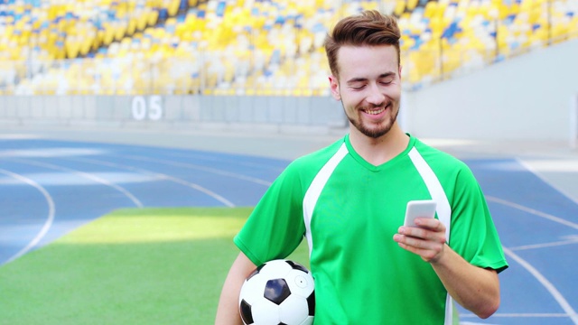 微笑的足球运动员拿着球和使用智能手机视频素材