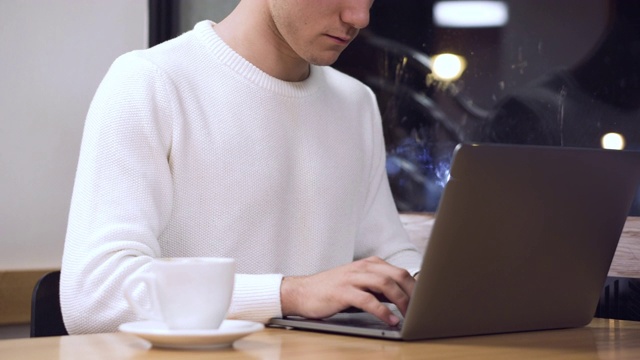 一个年轻人在咖啡店里用他的笔记本电脑工作，一个年轻的学生在电脑上打字。视频素材