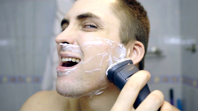 那家伙在浴室里用电动剃须刀刮胡子。那家伙在照镜子。视频素材