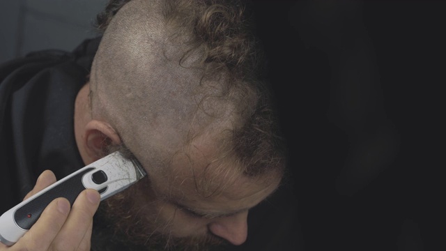 一个留胡子的男人用电动剃须刀剃头。留着胡子的朋克嬉皮士剃掉了他的莫霍克。男人剪他的头发。4 k的视频。59.94帧/秒视频素材