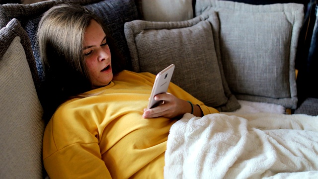快乐的女人用手机，早上在沙发上打哈欠视频素材