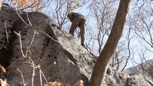 一个年轻人正在爬向巨石的顶端视频下载