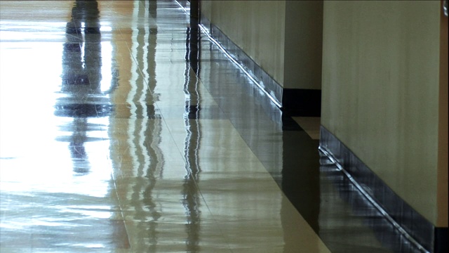 闪亮的打蜡地板映出一个男人走过走廊时的双腿。视频下载