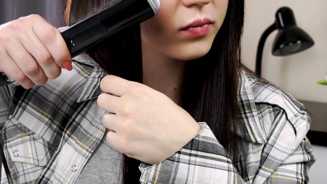 年轻漂亮的黑发姑娘用熨斗把头发拉直。头发护理视频素材