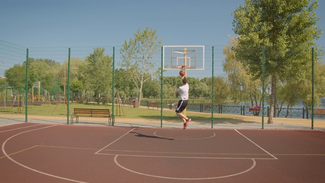 一个年轻的白人男性篮球运动员的特写，他在球场上向篮筐里扔球，背景是城市建筑视频下载