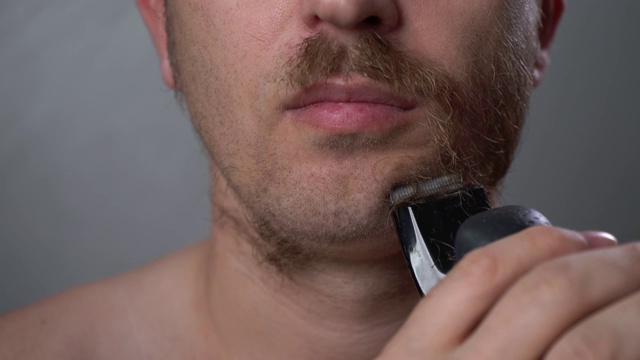 一个男人在家里用电动剃须刀刮胡子。视频素材