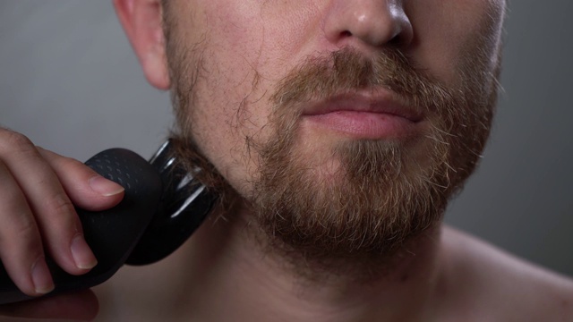 一个男人在家里用电动剃须刀刮胡子。视频素材