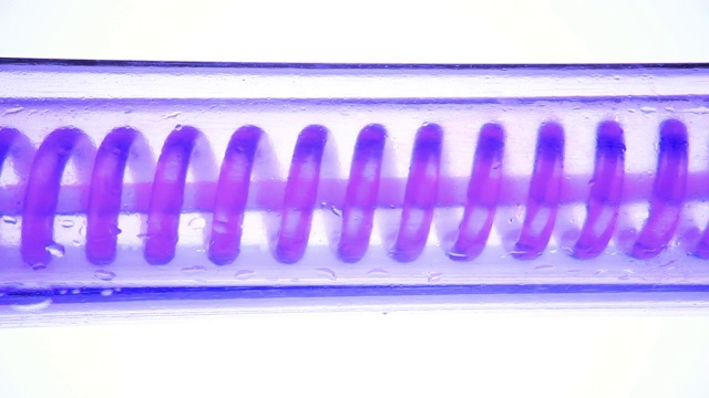 紫色和紫色的液体在流动，从左到右水平旋转。科学实验室冷凝器，关闭。科学实验室实验中的流体。彩色化学品通过冷凝器或玻璃管加工。冷却有机液体的过程。视频素材
