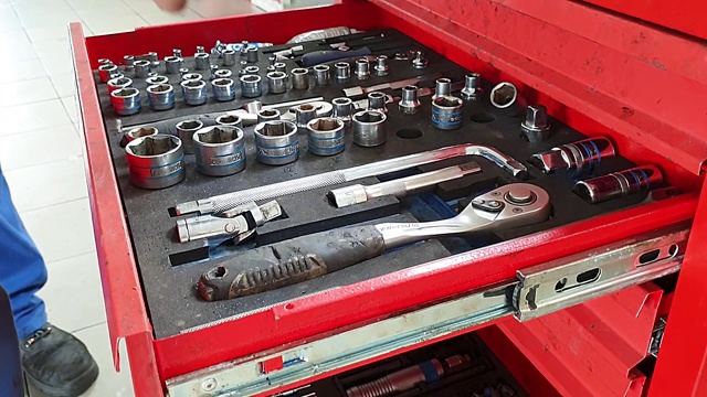 这个人把工具放进一个汽车车间的工具箱里的洞里，工具箱是红色的铁箱视频素材