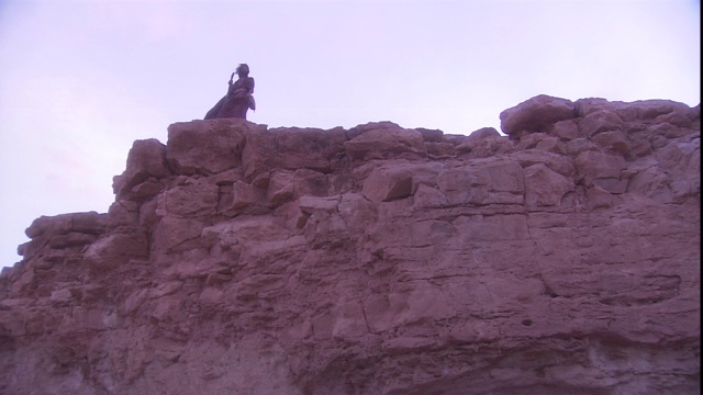 当一个人站在悬崖顶上时，风吹着他的长袍。视频素材