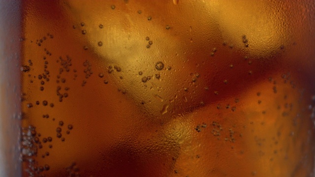 近距离拍摄的泡沫上升在可乐杯与冰。大量的含咖啡因的碳酸冰饮料视频下载
