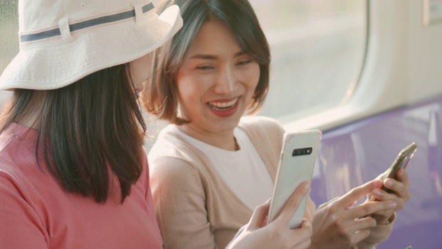 兩個年輕的亞洲女人在火車上一邊聊天一邊用手機，慢鏡頭視頻素材
