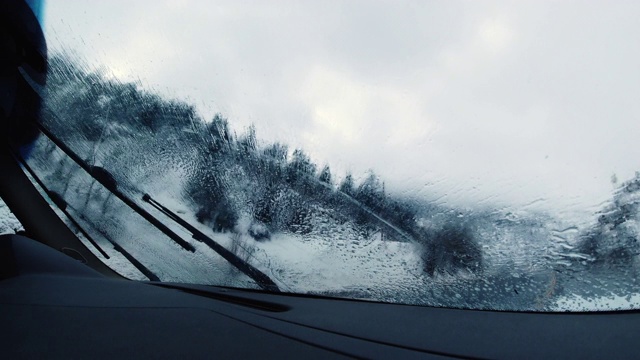 在阴天下的冬天，在大雪中行驶时，刮水器会清除汽车挡风玻璃上的水和冰视频购买