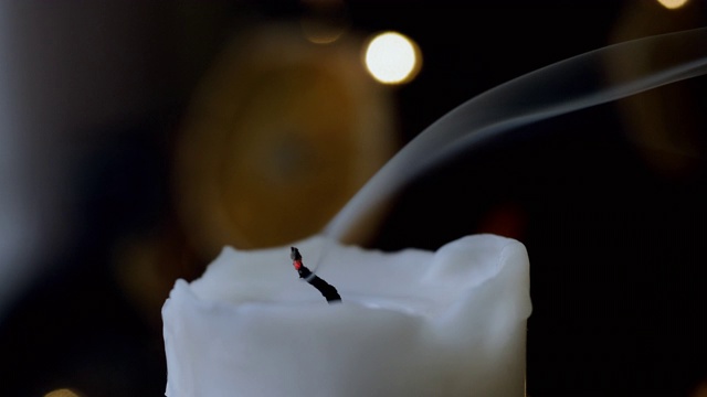 一个白色蜡烛在黑暗的背景燃烧的特写。蜡烛的火焰被吹灭了。4 k视频素材
