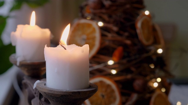 两支白色的圣诞蜡烛与冷杉树和模糊闪烁的灯光在背景。4 k视频素材