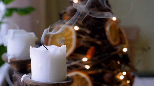 两支白色的圣诞蜡烛与冷杉树和模糊闪烁的灯光在背景。熄灭蜡烛的火焰。4 k视频素材