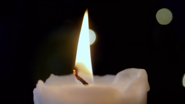 一个白色蜡烛在黑暗的背景燃烧的特写。4 k视频素材