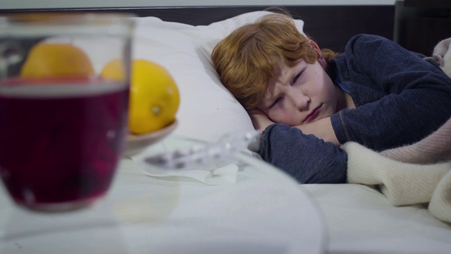 生病的白人可爱男孩躺在床上吃药的特写。一个可怜的红发小孩周末呆在家里。疾病、医疗、医学。视频素材