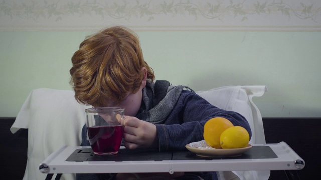 一个患流感的白人红发小孩一边喝着茶一边坐在床上。可爱不安不健康的孩子呆在家里。医学、疾病、医疗保健。视频素材