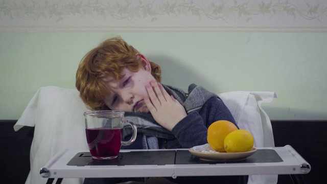 前视图肖像生病的高加索男孩有温度。悲伤可爱的孩子坐在床上，面前放着茶和橘子。疾病、医疗、医学。视频素材
