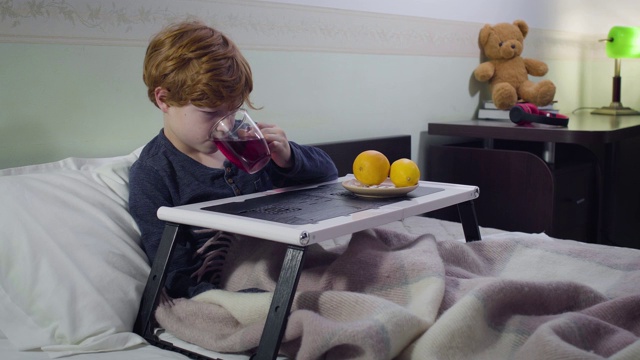 可怜的红发白人男孩躺在床上喝着热果茶。卧病在床的孩子的肖像。医疗、医药、疾病。视频素材