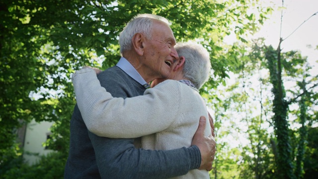 在一个阳光明媚的绿色公园里，一对老年夫妇深情地拥抱着以示他们永远的爱和尊重视频下载