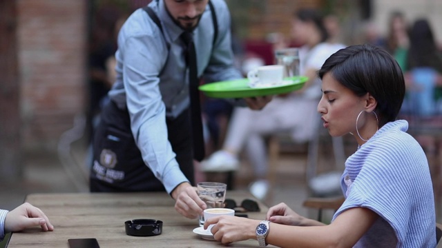 年轻夫妇在户外咖啡馆放松和聊天，服务员为他们提供咖啡视频下载