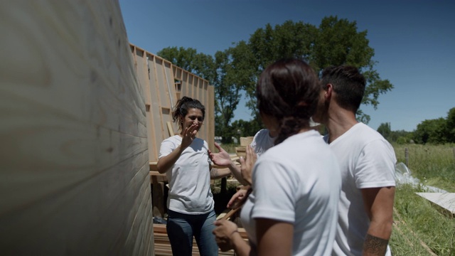 一群志愿者加入一对夫妇试图举起一个慈善建筑工地的沉重木墙视频下载